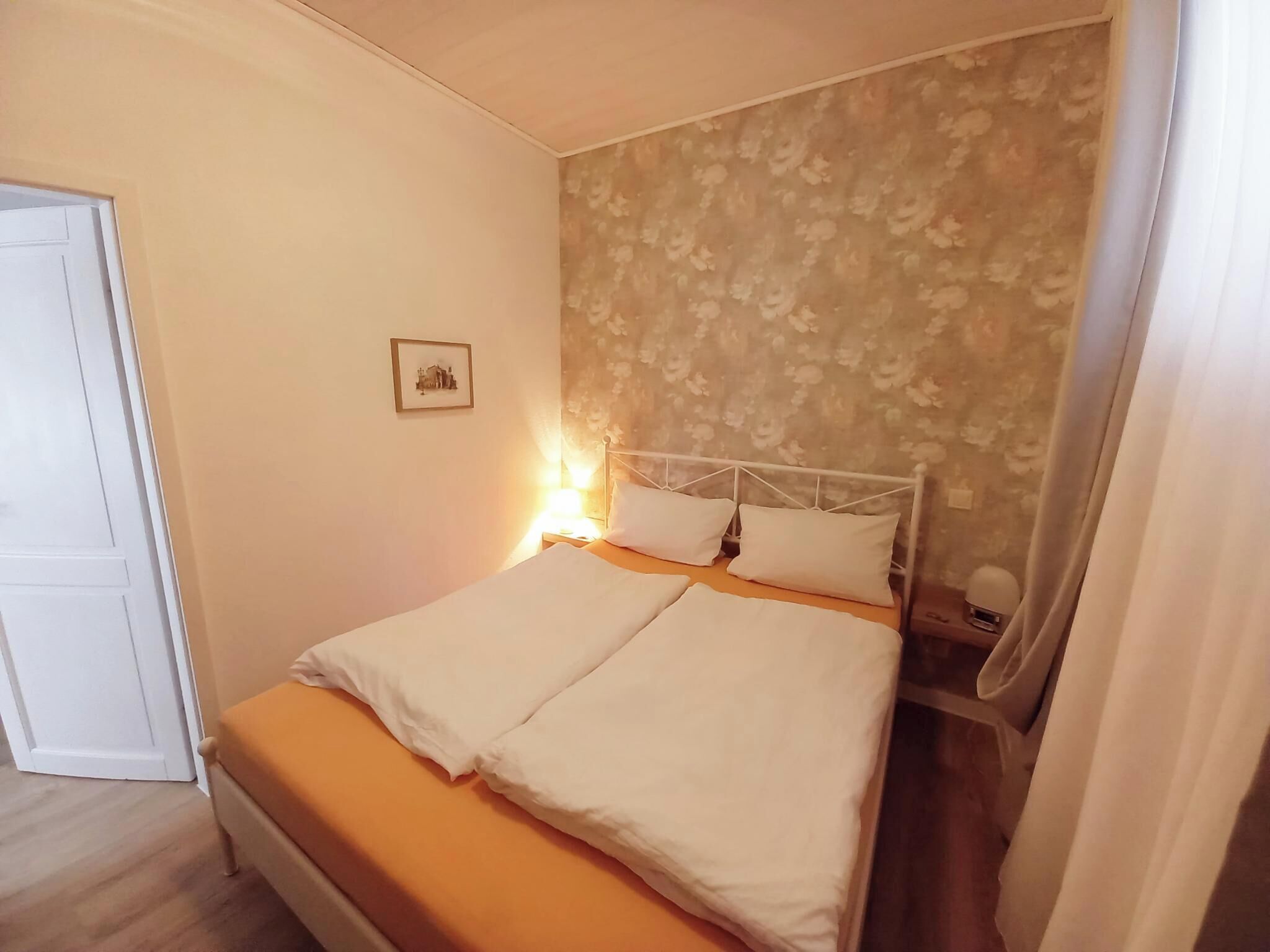 A bedroom with a bed, a nightstand, a lamp, and a framed picture on the wall.