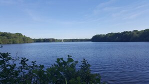 A calm lake with a sailboat in the distance, surrounded by dense forest. - Feel-good apartment in the preferred south of Duisburg for business and Private travelers (Duisburg)