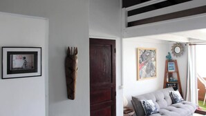 Una habitació amb un quadre emmarcat, un penjall decoratiu, un sofà amb coixins i una porta.