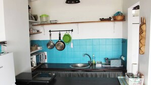 Cuina compacta amb taulell negre, una aixeta i un microones. Hi ha olles penjades i una estant amb articles de cuina.