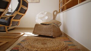 Une pièce avec un tapis tissé, un pouf rond tissé, un repose-pieds tissé et une chaise en bois.