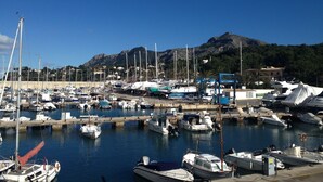 Un port de plaisance où sont amarrés différents types de bateaux, un ciel dégagé et un paysage montagneux en arrière-plan.