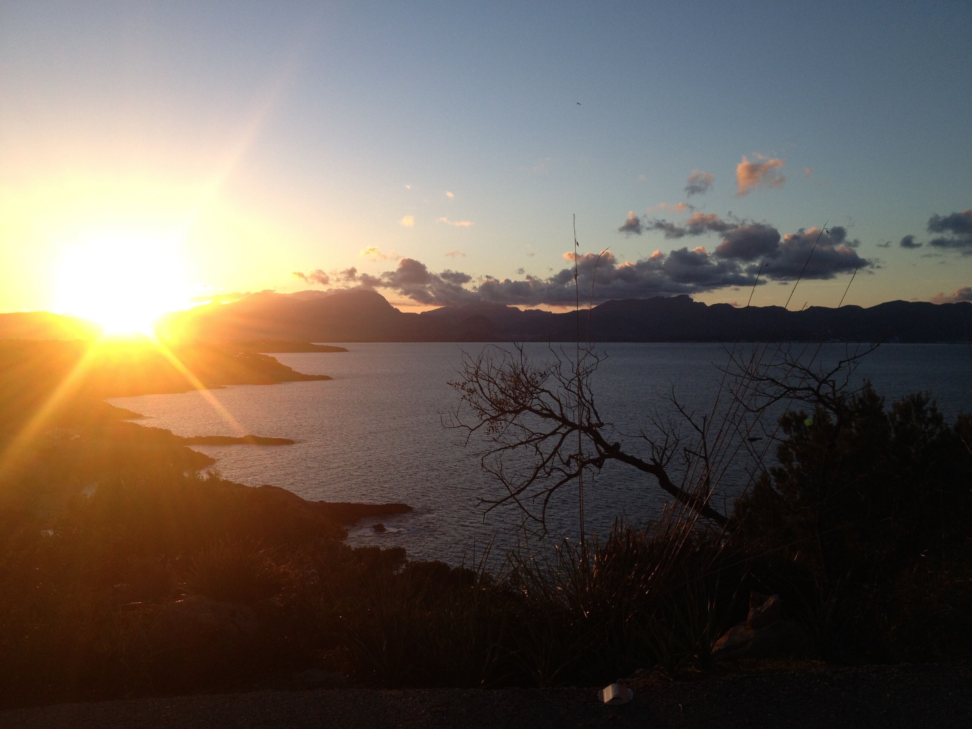 Solnedgang over vand med bjerge i baggrunden.