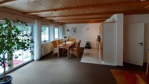 A spacious room with a wooden ceiling, a dining area with a table and chairs, a potted plant, and a view of the outdoors through large windows. - Pure vacation. Arrive and feel good, 2-5 pers. 80sqm, terrace, 2 bedrooms. W-lan (Walkenried)