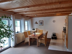 A cozy dining area with a wooden table and chairs, a window with curtains, a wall-mounted clock, and a kitchen area with cabinets and appliances. - Pure vacation. Arrive and feel good, 2-5 pers. 80sqm, terrace, 2 bedrooms. W-lan (Walkenried)