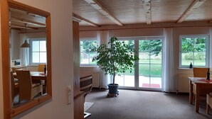 A room with a wooden ceiling, large windows, a potted plant, and a dining area with a table and chairs. - Pure vacation. Arrive and feel good, 2-5 pers. 80sqm, terrace, 2 bedrooms. W-lan (Walkenried)