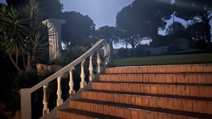 Un escalier orné d’une balustrade mène à un bâtiment, qui est entouré d’arbres et se dresse sous un ciel dégagé.