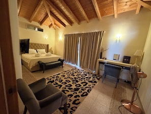A hotel room with a bed, a desk, a chair, a leopard print rug, and a ceiling with wooden beams.