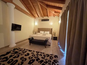 Une chambre d’hôtel avec un lit, un téléviseur à écran plat, un banc, un tapis à motifs et une fenêtre avec des rideaux.