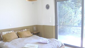 Une chambre avec un grand lit, une table de chevet, une lampe et une vue sur l’extérieur grâce à une porte coulissante.