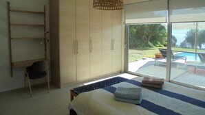 Une chambre dotée d’un grand lit, d’une armoire, d’un bureau et offrant une vue sur une piscine et un espace verdoyant.