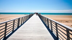A wooden pier leading to a beach with clear skies.