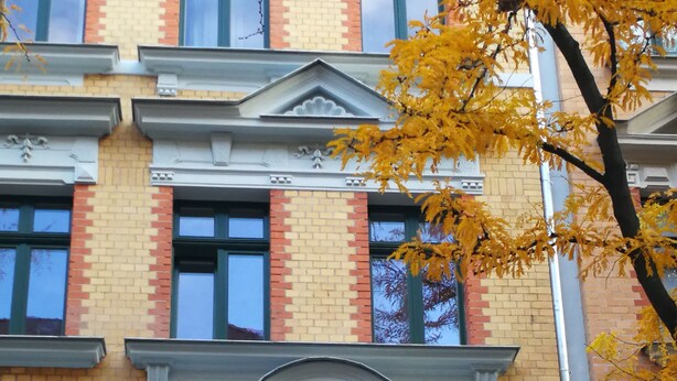 Un bâtiment à la façade symétrique, ornée d’un élément décoratif central au-dessus des fenêtres et d’un motif en briques rouges et jaunes.