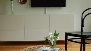 Un salon comprenant un pouf en osier, un téléviseur à écran plat fixé au mur, un meuble blanc et un fauteuil noir.