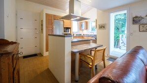 A compact kitchen with wooden cabinets, a central island, and a dining area with a chair.