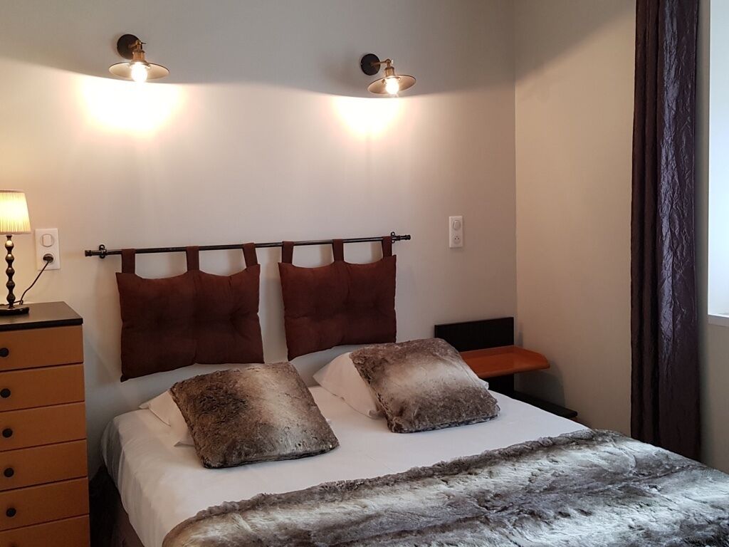 Ein Schlafzimmer mit einem Bett, zwei Wandleuchten, einer Kommode und einem Fenster mit Vorhängen.