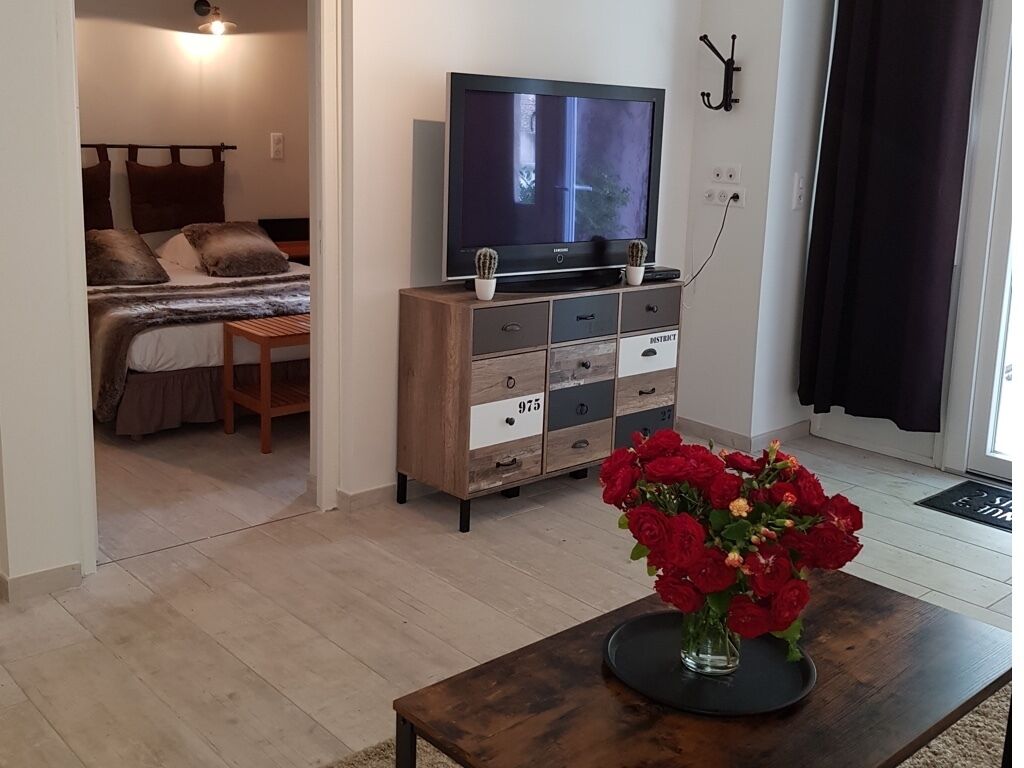 Ein Schlafzimmer mit einem Bett, einem Fernseher auf einer Holzkommode und einer Vase mit roten Blumen auf einem Tisch.