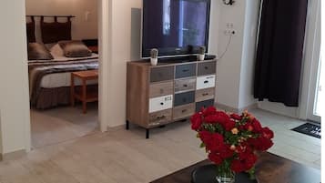 Ein Schlafzimmer mit einem Bett, einem Fernseher auf einer Holzkommode und einer Vase mit roten Blumen auf einem Tisch.