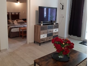 A bedroom with a bed, a TV on a wooden cabinet, and a vase of red flowers on a table.