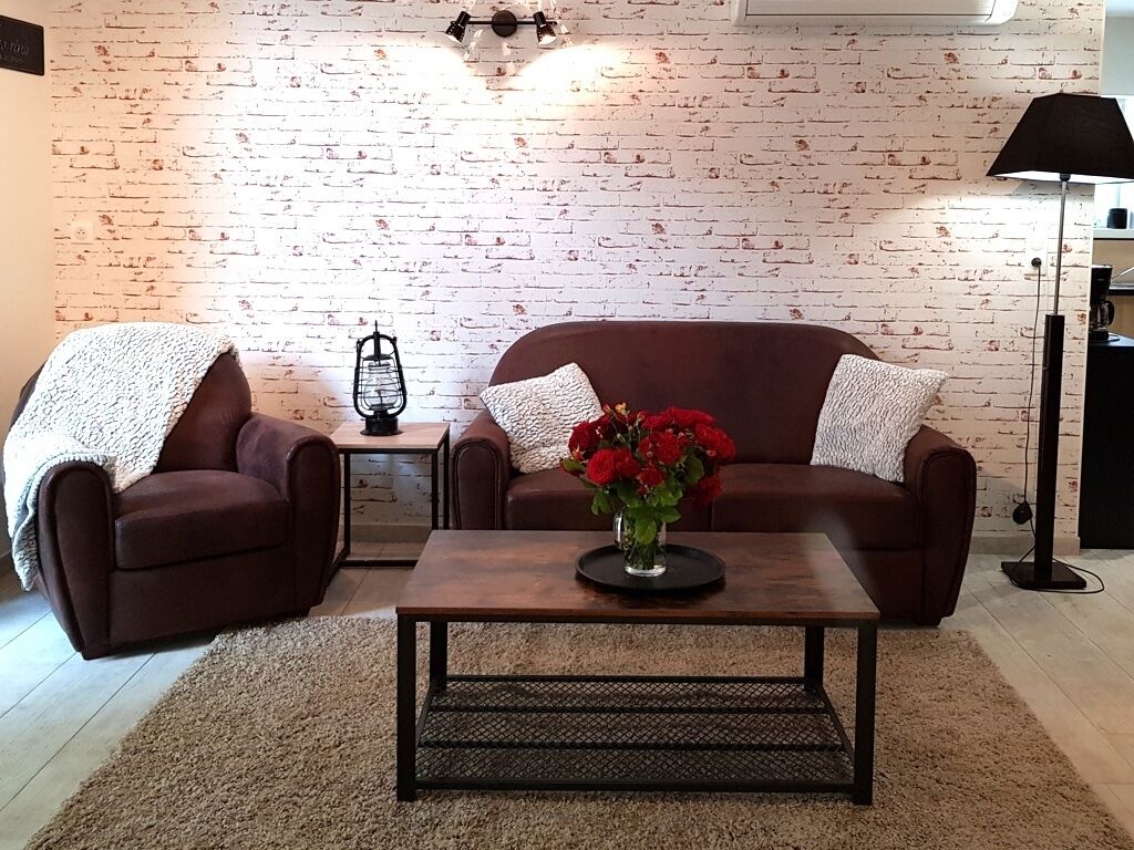 Een woonkamer met een bakstenen muur, twee bruine banken, een salontafel en een lamp.