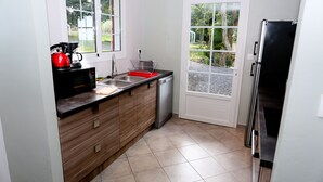 Una cocina compacta con lavavajillas, un hervidor rojo y un lavabo.