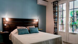 Un dormitorio con cama, mesitas de noche, lámpara en el techo y ventana con cortinas.