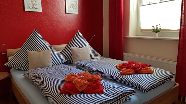 A double bed with striped bedding and red towels, a red wall with decorative elements, and a window with a view. - Apartment 'Am Poeler Tor' in the old town of Wismar (Wismar)