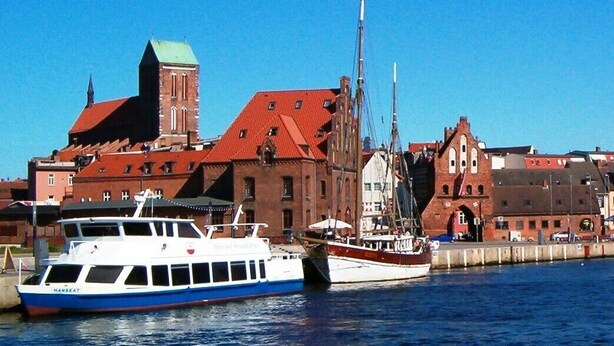 A harbor with a large red-roofed building, a white boat named 'NANBEAT', and another boat docked nearby. - Apartment 'Am Poeler Tor' in the old town of Wismar (Wismar)