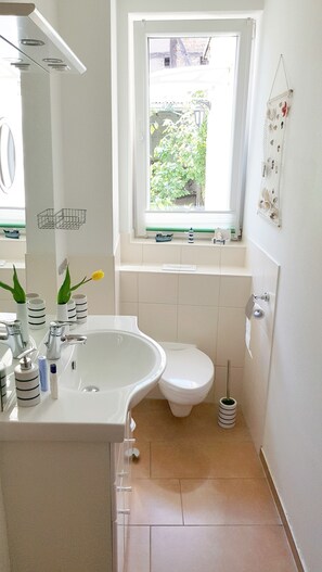 A small, clean bathroom with a white sink, toilet, and a window above the sink.