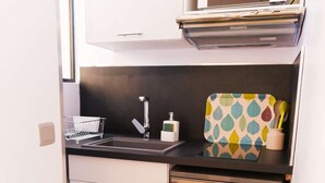 A compact kitchen with a microwave, a small refrigerator, a sink with a faucet, and a patterned utensil holder. - Studio Premium Toulouse Zénith - Parking,  Métro et Netflix (Toulouse)