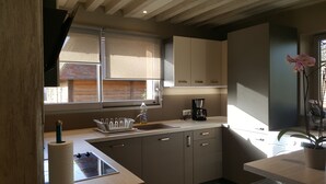 A modern kitchen with a built-in stove, a sink, and a coffee maker. There is a window with blinds, a potted plant, and a view of the outside. - AN INDEPENDENT HOUSE FOR 4 PEOPLE AT PONT L'EVEQUE, BETWEEN HONFLEUR AND DEAUVILLE  (Coudray-Rabut)