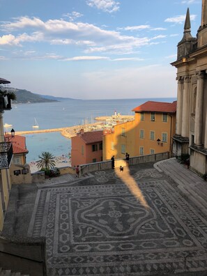 A coastal town with a view of the sea, a patterned pavement, and buildings with balconies.
