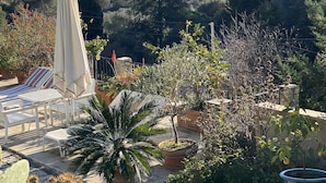 A patio area with outdoor furniture, potted plants, and a view of a bridge and hills in the background. - Rest and nature in Menton, sea and private pool. Pet-friendly. (castellar)