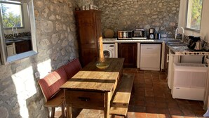 A rustic kitchen with stone walls, a wooden table, and a built-in oven. - Rest and nature in Menton, sea and private pool. Pet-friendly. (castellar)