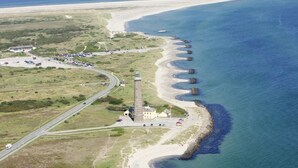 An aerial view of a coastal area with a lighthouse, a road, and a beach.