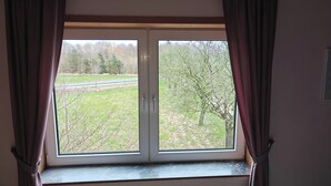 A room with a large window, curtains, and a view of a grassy area with trees.