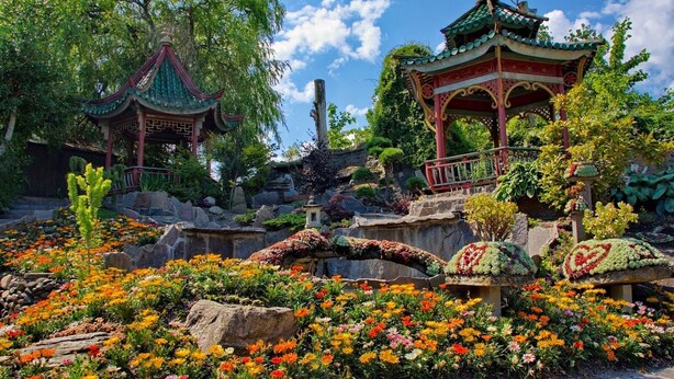 A traditional Chinese pavilion surrounded by colorful flowers and rocks.