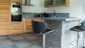 Cocina moderna con armarios de madera, horno integrado y barra con taburetes.