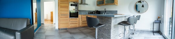 Une cuisine moderne avec des meubles en bois, un four encastré et un coin bar avec des tabourets.