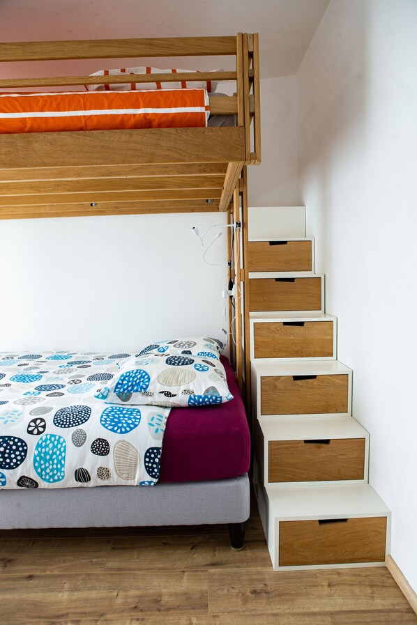 Una cama litera con un edredón estampado, una colcha morada y una escalera de madera con cajones de almacenamiento.