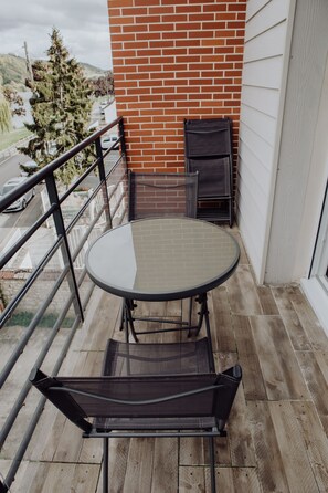 A balcony with a round table and two chairs, a brick wall, and a view of a street and trees.