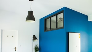 Una sala de estar moderna con una pared azul de acento, un sofá gris, una lámpara colgante y una puerta blanca.