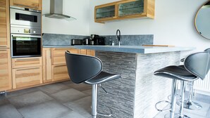 Una cocina moderna con armarios de madera, electrodomésticos de acero inoxidable, encimera de mármol y dos taburetes de bar.