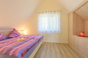 Une chambre à coucher avec un lit, une lampe de chevet, une fenêtre avec des rideaux légers et une armoire en bois.