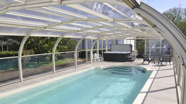 A covered swimming pool with a glass roof, surrounded by a patio area with outdoor furniture. - HOUSE 4 PERS + SPA + HEATED POOL CALM & REST IN MARAIS POITEVIN VENDEE (Liez)