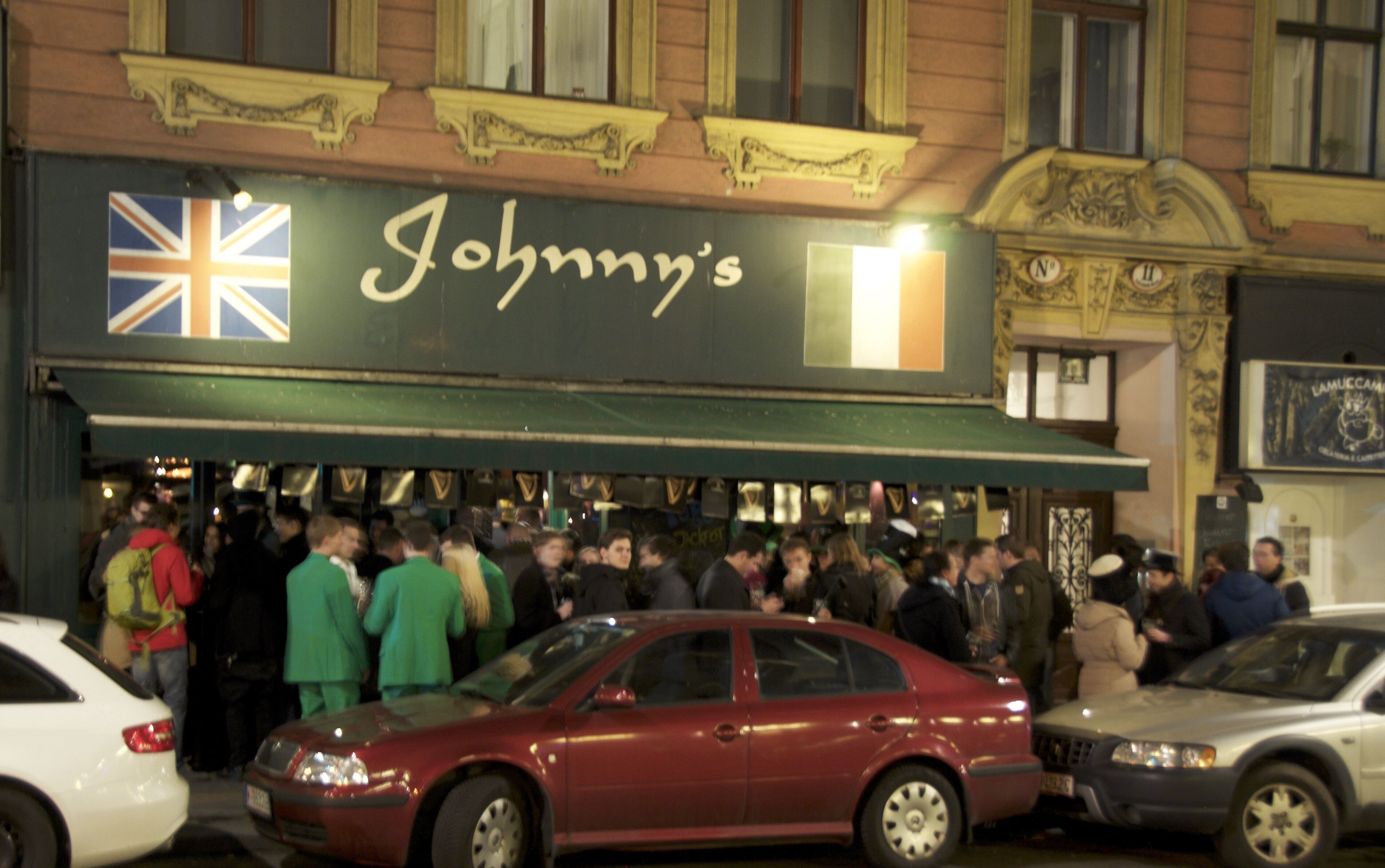 Escena de calle concurrida frente a un edificio con un letrero que dice 'Johnny's'.
