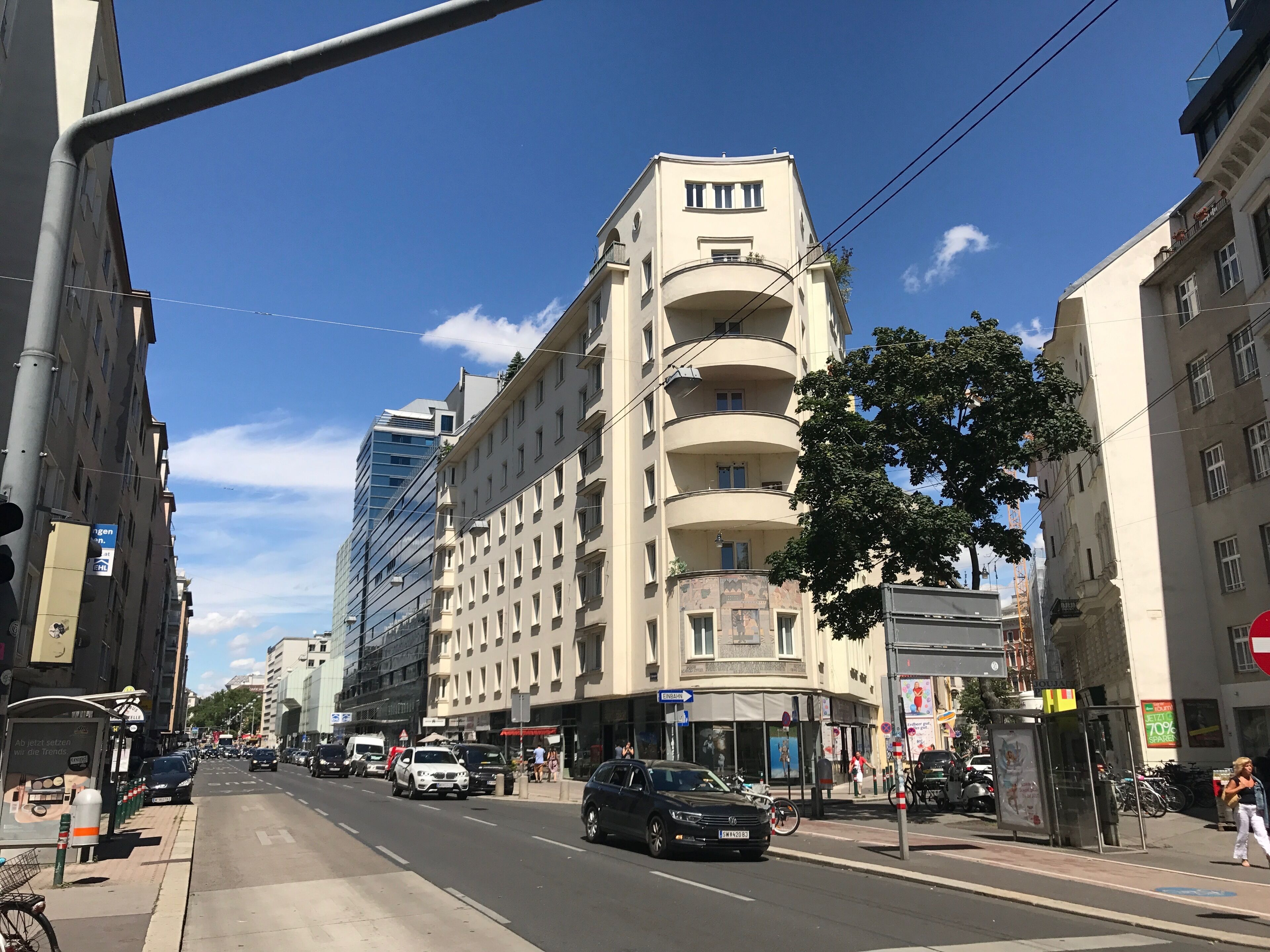 A multi-story building with a curved facade, a bus stop, and a clear blue sky.