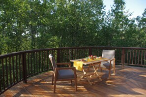 A wooden deck with a table and chairs, surrounded by a wooden railing, set against a backdrop of dense green trees. - The Cabane Rouge-Gorge (Auriac-Du-Périgord)