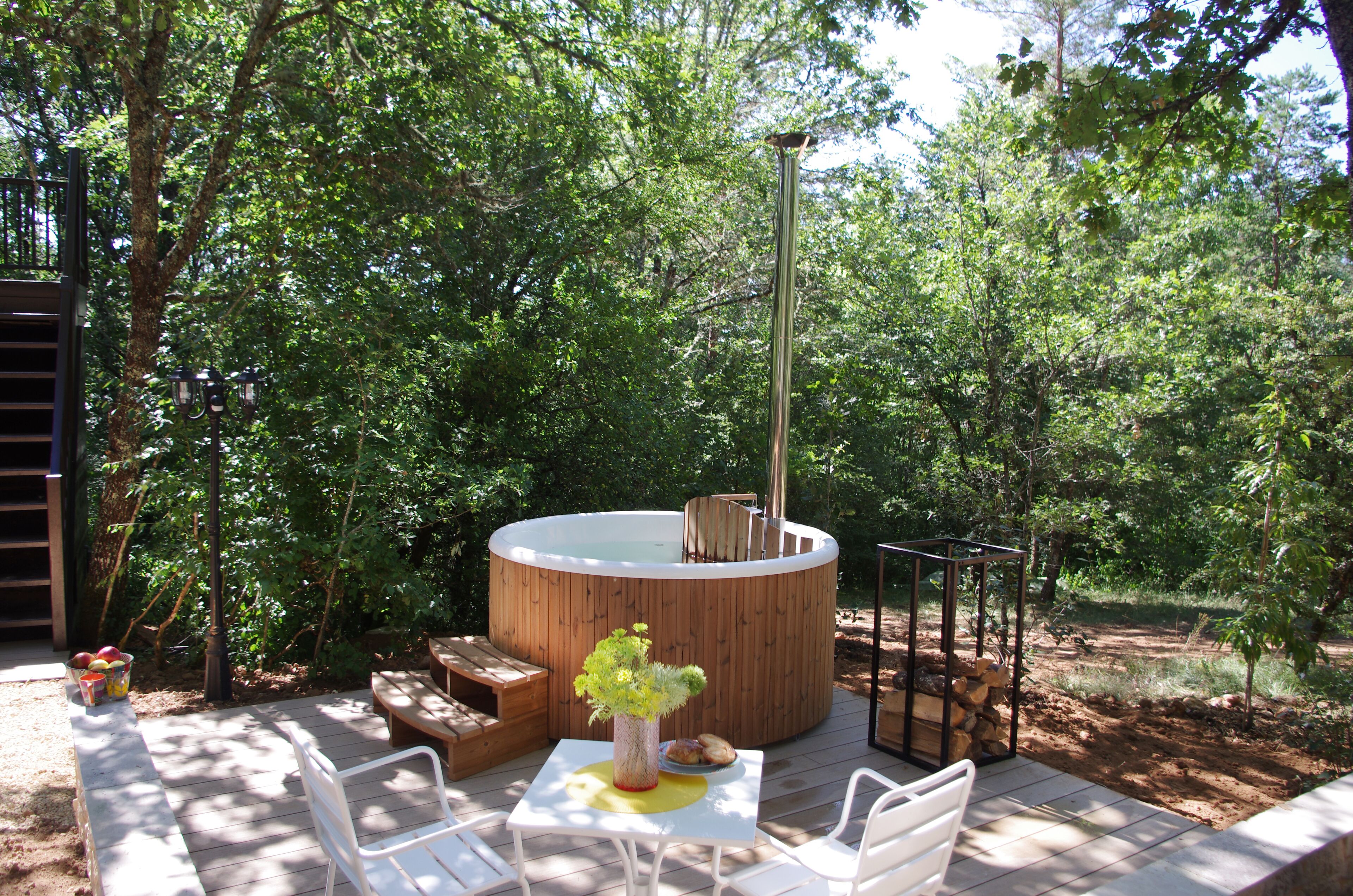 Un bain à remous entouré d’une terrasse en bois, avec une table et des chaises à proximité.