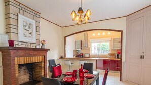 A dining area with a brick fireplace, a chandelier, and a view into a kitchen with red cabinets and a window. - Large atypical charming house entirely renovated. (Jonzac)